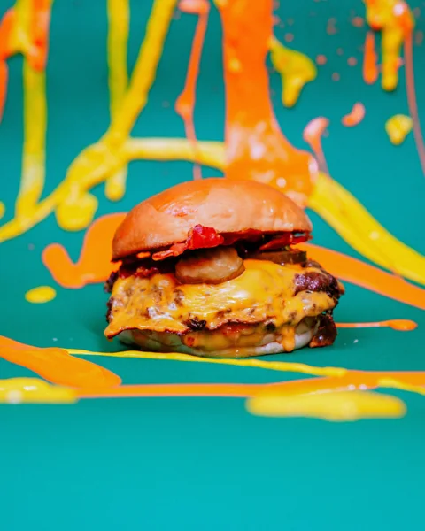Burger su sfondo verde petrolio con schizzi di vernice